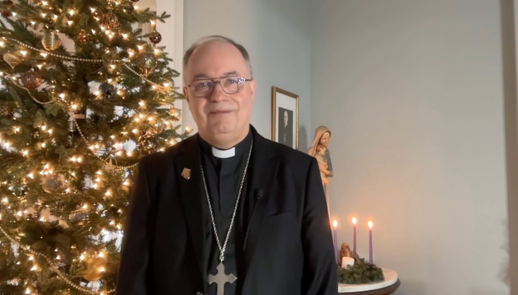 Bishop standing in front of a Christmas tree and Advent wreath.